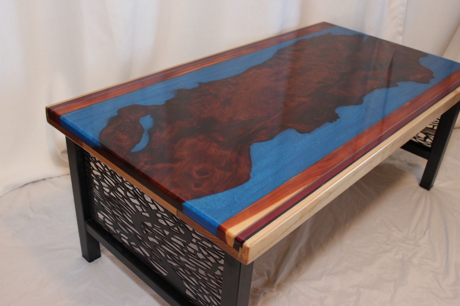 Custom coffee table and custom base. Redwood burl, with blue epoxy, maple, red cedar and purple heart border. Traditional table top epoxy finish. ~44″x24″